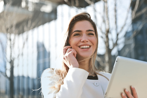 woman in white blazer holding tablet computer and phone